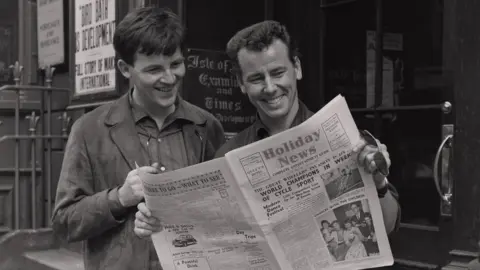 MNH Black and white photograph of two men looking at a newspaper