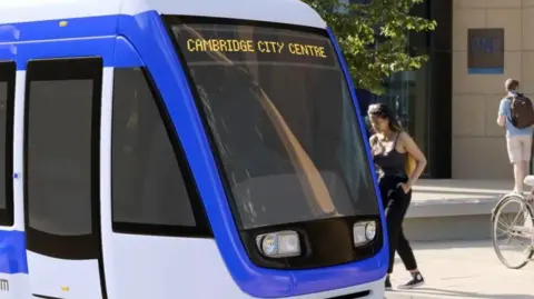 Cambs & Peterborough CA Illustrative image of the CAM, a tram-like vehicle which has "Cambridge City Centre" written on the top and a woman appearing to get on.