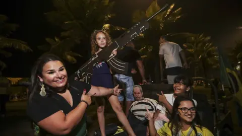 EPA A girl posses for a photograph holding a gun made of paper as supporters of Brazilian far-right presidential candidate Jair Bolsonaro celebrate his victory