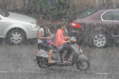 Getty Images Indian women commute on a two wheeler during a heavy down pour of rain in Hyderabad on July 28, 2010.