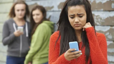 Thinkstock Girl receiving a nasty message with girls in background