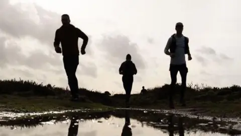 The silhouette of three men running through the countryside.