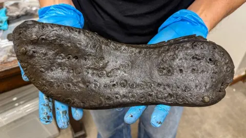 The bottom of a large shoe, being held by a woman wearing blue plastic gloves
