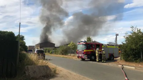 Shaun Whitmore/BBC Firefighters tackling the flames at the site in Weeting