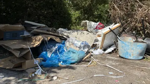 Large pile of rubbish including cardboard, plastic, carpets, wooden frames.