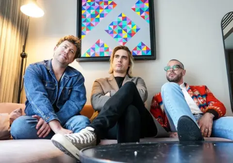 PA Media Busted musicians James Bourne, Charlie Simpson and Matt Willis sitting on a couch