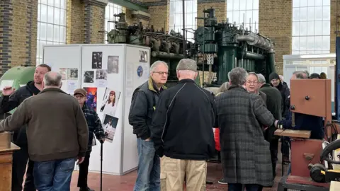 TOM LARSEN-WRIGHT/BBC Small groups of men engage in conversation in front of two ten foot water pump engines