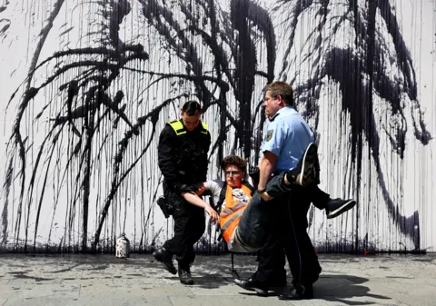 CHRISTIAN MANG / Reuters Police officers remove an activist of the "Letzte Generation" (Last Generation) after they spilled black liquid, symbolizing oil during a protest in Berlin, Germany, 22 June 2022.