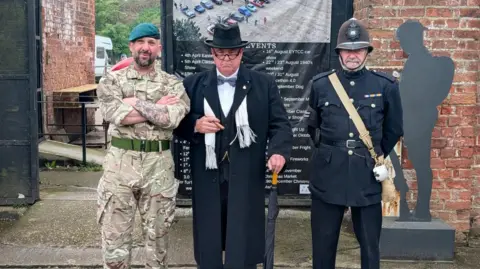 Three men dressed in different outfits - one as a Royal Marine wearing a green beret, one as Winston Churchill, and another in a vintage police officer uniform.