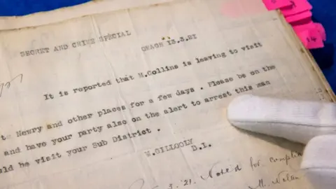 PA Media Auctioneer Karl Bennett points on a page from a large dossier of Royal Irish Constabulary (RIC) documents with a notice to arrest Michael Collins