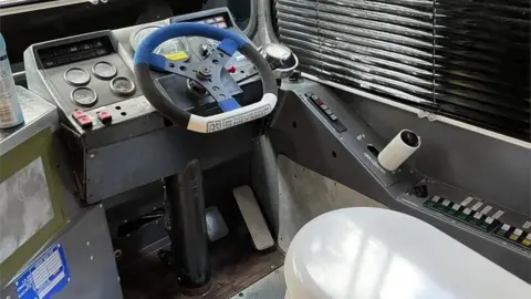 Ann Cooper Driver's cab of a bus with the seat replaced by a toilet