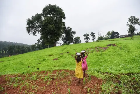 WaterAid/Ronny Sen Twin sisters carry water back to their home.
