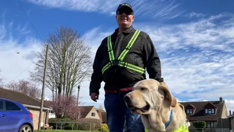 BBC Alex Gosney walking on the street with his guide dog Homer