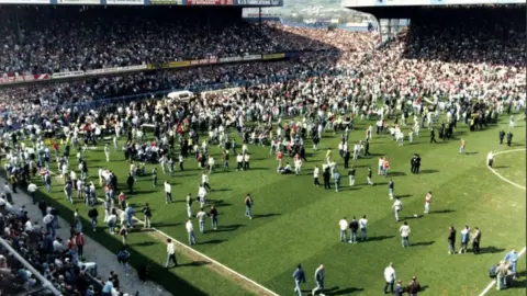 Fans on the pitch alongside a lone white ambulance near the goalmouth after the crush at the FA Cup semi-final