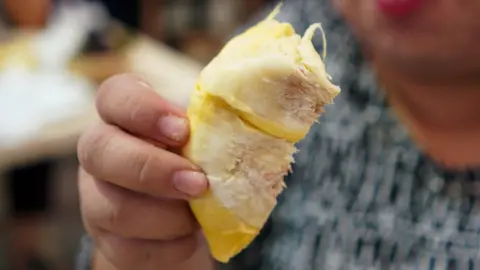 Reuters A woman eats a durian at a department store in Bangkok, Thailand on 26 April 2018