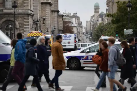 AFP Passerby walk as police vehicle drive toward Paris after a fatal knife attacks.