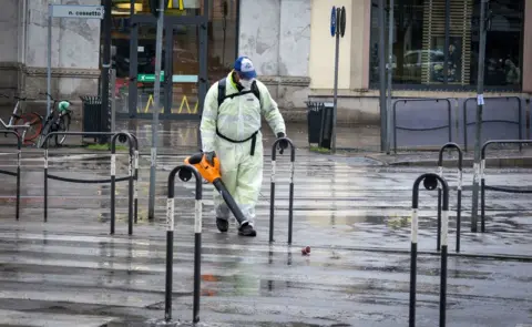 Getty Images A man in overalls and sanitary equipment works in a street