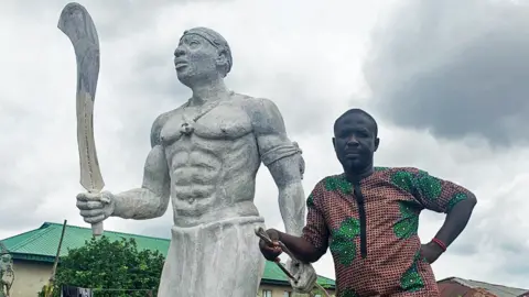 BBC Monday Aigbe standing alongside a statue of his great-grandfather