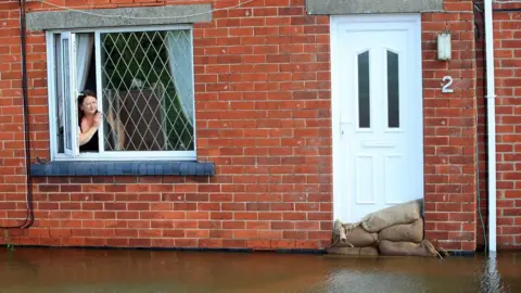 PA Woman looking out a window of a house, which is surrounded by floodwater