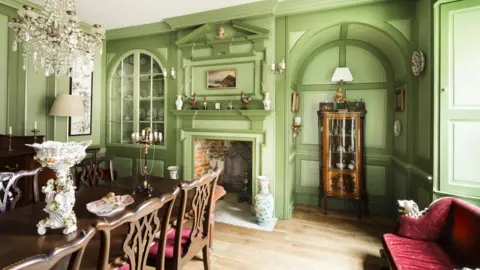 Historic England The manor house dining room. It has green walks, some of which is panelled and an open fireplace.