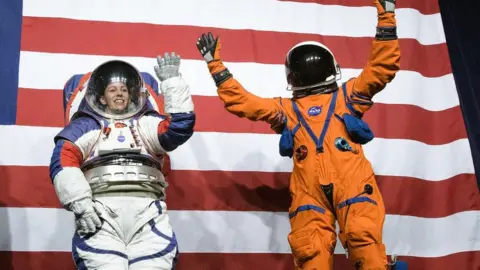 NASA Kristine Davis, a spacesuit engineer at NASA’s Johnson Space Center, wearing a ground prototype of NASA’s new Exploration Extravehicular Mobility Unit (xEMU), and Dustin Gohmert, Orion Crew Survival Systems Project Manager at NASA’s Johnson Space Center, wearing the Orion Crew Survival System suit, right, wave after being introduced by the administrator, Tuesday, Oct. 15, 2019 at NASA Headquarters in Washington