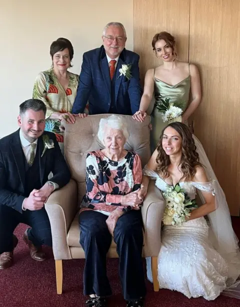 Family handout Hannah and her family wearing their wedding outfits alongside Liz Jobey