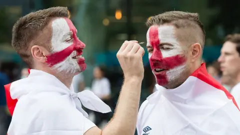 England football fans paint their faces as they arrive at Wembley Stadium ahead of England match against Denmark in the semi-final of Euro 2020 Championship