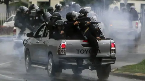 AFP Dozens of heavily armed police ride in the backs of trucks, shotguns at the ready, through the streets