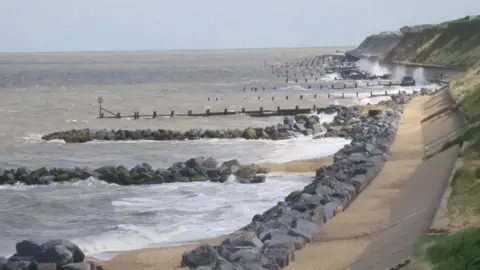 Brian Hardisty Waves crash against sea defences including rocks and groynes on a sunny day