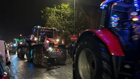 Tractors decorated in flashing lights driving along a road in the dark