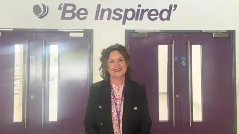 North Northamptonshire Council A woman is smiling near two sets of purple double doors with the words "Be inspired" written in purple font on the wall behind her.