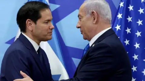 Marco Rubio shakes hands with Benjamin Netanyahu in front of US and Israeli flags.