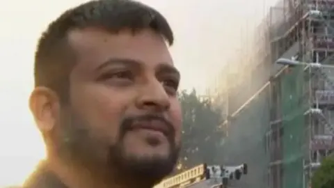 Dinesh Raj, a bearded man, standing in front of the Dagenham tower block after the fire