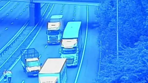 View from a motorway bridge showing lorries stopped and police officers standing on the carriageway