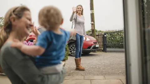 Getty Images stock image - A women waves goodbye to her mother and son from across the street as she leaves the house.