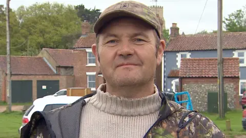 Shaun Whitmore/BBC Gardener Jonathan Wright seen with cap and in front of a row of houses