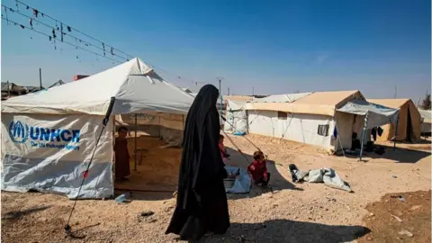 Getty Images A woman walks past tents at the al-Hol camp in Syria