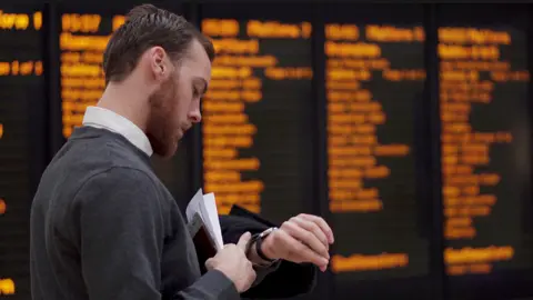 Getty Images Man checks watch at train station