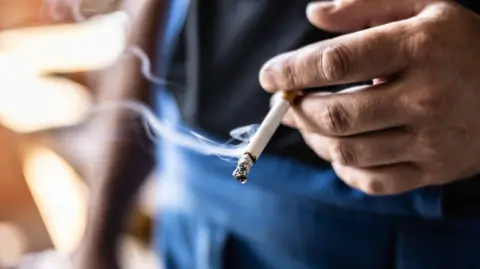 A stock image of someone's hand holding a lit cigarette.