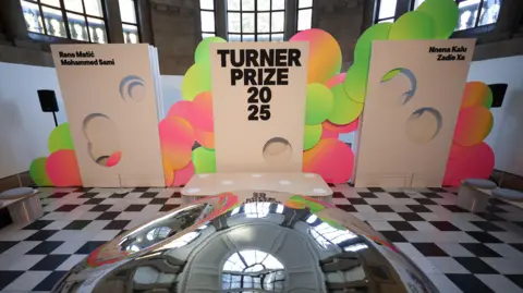 EPA/Shutterstock Three signs saying Turner Prize 2025 in a gallery with a chequered floor