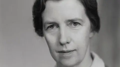 Dame Mary Cartwright is seen looking at the camera in a black and white photo. It is a close-up of her face and she has dark hair that is tied back.