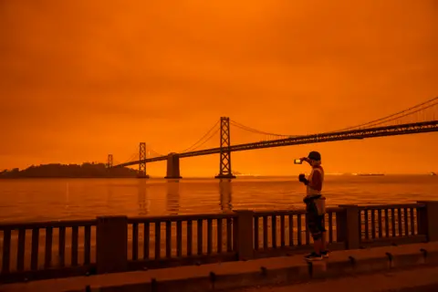 Philip Pacheco / Getty Images A woman takes in the view from the Embarcadero as smoke from various wildfires blankets San Francisco in darkness and an orange glow on 9 September 2020