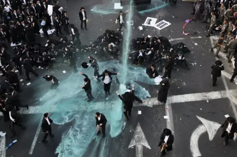 ABIR SULTAN/ EPA Ultra-Orthodox Jews are hit by a water canon.