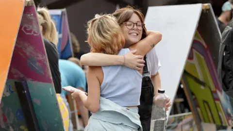 Plaster Communications Two women who are painting canvases at Upfest Presents in Bristol embrace