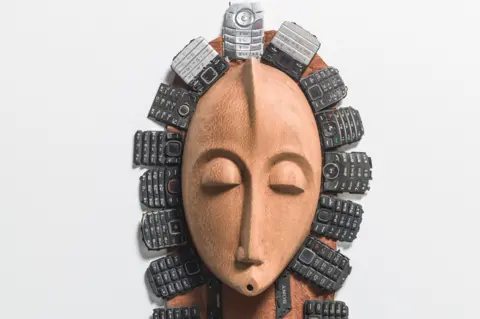 Steve Russell Studios A Peter Oloya artwork, which features a traditional bride mask adorned with keypads of old mobile phones