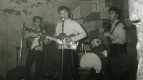 Tracks Ltd/PA John Lennon and Sir Paul McCartney at the microphone, with George Harrison on guitar and a partially obscured Pete Best, the group's original drummer