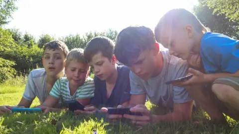 Getty Images Children of varied ages looking at screens outdoors