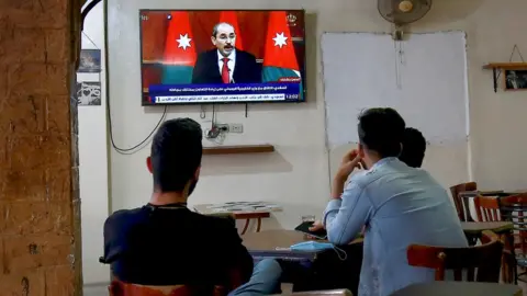 Getty Images Jordanians follow the latest political developments in their country on a television set at a cafe in the capital Amman