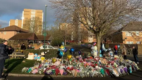 PA Media Flowers and tributes lay near to the scene in Babbs Mill Park in Kingshurst, Solihull