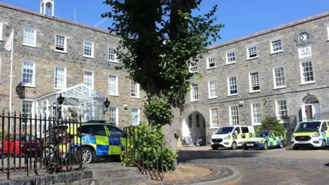 BBC A view of Guernsey Police station. Showing the brick building and police cars parked outside.